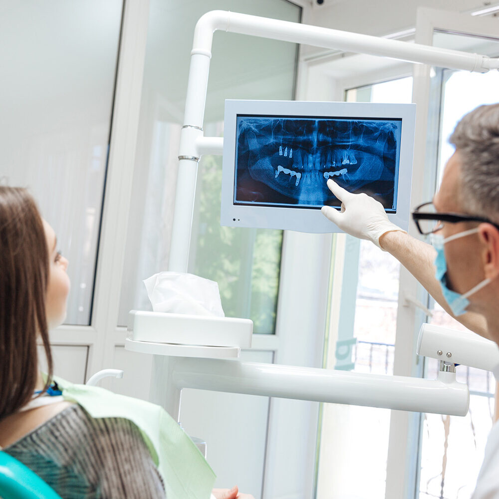 Male dentist shows a patient x-ray of teeth in clinic